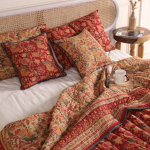 Può includere: Set di biancheria da letto con trapunta a fantasia floreale rossa e beige e cuscini coordinati. I cuscini hanno un bordo verde. La trapunta e i cuscini sono su un letto bianco con testiera intrecciata.
