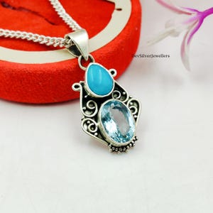 Puede incluir: Un collar con colgante de plata con una piedra turquesa en forma de lágrima sobre una piedra ovalada azul claro. El colgante tiene un diseño ornamental y de filigrana. El texto "DevSilverJewellers" es visible.