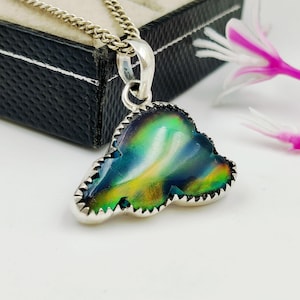 May include: A silver pendant with a colorful, iridescent stone. The stone has shades of green, blue, and yellow. The pendant is on a silver chain. The stone is framed by a silver, scalloped edge.
