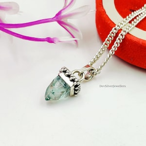 Op de afbeelding: Een zilveren ketting met een lichtblauwe kristallen hanger. De kristal is gezet in een decoratieve zilveren zetting en hangt aan een zilveren ketting. De hanger heeft een unieke, puntige vorm.