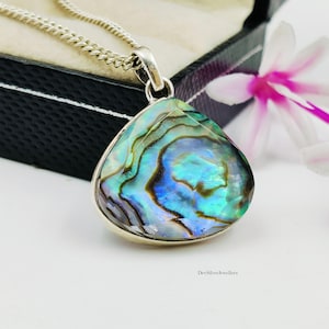 May include: A silver pendant necklace featuring a teardrop-shaped abalone shell inlay with iridescent blue, green, and purple swirling patterns. The pendant hangs from a silver chain, and the text DevSilverJewellers is visible at the bottom.