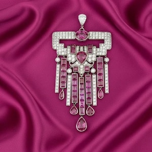 Könnte beinhalten: Ein Anhänger mit geometrischem Design, mit klaren und rosa Edelsteinen. Der Anhänger hat eine rechteckige Oberseite mit einem zentralen ovalen rosa Stein und einem tropfenförmigen rosa Stein unten. Auf tiefrosa Stoffhintergrund.