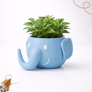 Peut inclure: Un pot de fleurs bleu clair en forme d'éléphant avec un visage souriant et des détails blancs. Le pot est rempli de plantes vertes. L'éléphant a une trompe et de grandes oreilles. Un article décoratif amusant et fantaisiste.