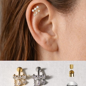 Peut inclure: Bijoux de perçage d'oreille dorés et argentés avec des accents de cristaux pendants. Les bijoux sont présentés sur une oreille et également affichés séparément. Les bijoux ont une tige et un dos vissé. Les bijoux sont en titane.