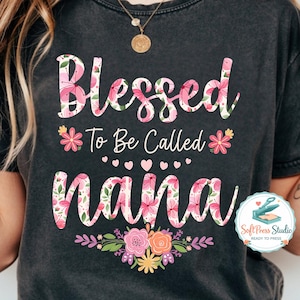 May include: Dark gray t-shirt with the words "Blessed To Be Called Nana" in a floral design. The word "Blessed" is in large, cursive letters with a pink floral pattern. The word "Nana" is also in a floral design.