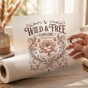 May include: A translucent sheet of vellum paper featuring a brown ink illustration of a large peony flower, butterflies, and stars. The text reads WILD & FREE, EXPLORE, and ADVENTURE AWAITS. A small circular wax seal stamp with a crescent moon is visible.