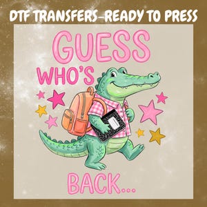 May include: A DTF transfer design featuring a green cartoon alligator wearing a pink plaid shirt, carrying an orange backpack and a black composition notebook. The text reads DTF TRANSFERS-READY TO PRESS, GUESS WHO'S BACK, surrounded by pink and yellow stars.