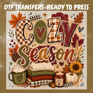 May include: A DTF transfer graphic featuring the text COZY SEASON with a heart replacing the O. The design includes autumn leaves, a stack of folded sweaters, a green mug with whipped cream, a sunflower, a pumpkin, and a candle labelled COZY VIBES.