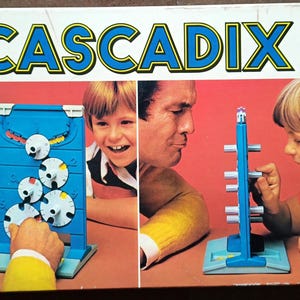 May include: A vintage CascadiX board game box. The box displays the game's name in large blue letters, with images of people playing the game. The game seems to involve manipulating circular pieces on a blue board. The box is rectangular.