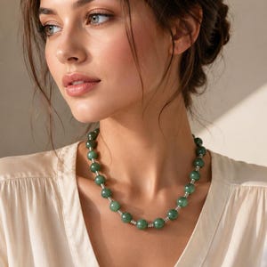 Puede incluir: Un collar de cuentas con grandes cuentas redondas verdes. Las cuentas están intercaladas con pequeños espaciadores plateados. El collar se lleva alrededor del cuello y las cuentas son de un color verde intenso.