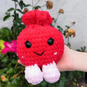 Può includere: Un peluche rotondo all'uncinetto di colore rosso brillante con una superficie in filato testurizzato. Presenta due grandi occhi di sicurezza neri lucidi, un sorriso nero ricamato e due piccoli accenti bianchi sulle guance. Due piedini rosa chiaro e soffici sporgono dal basso.