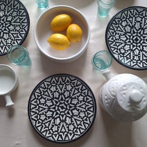 Puede incluir: Vista aérea de una mesa con platos estampados en blanco y negro, vasos turquesa pequeños y un cuenco blanco con tres limones. También hay una fuente blanca.