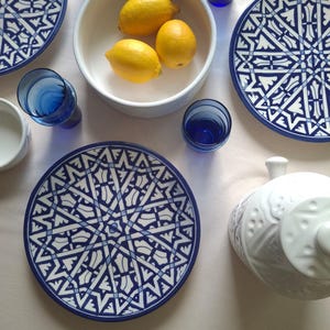 Op de afbeelding: Luchtfoto van een tafelsetting met wit en blauw gedessineerde borden, blauwe glazen, een witte kom met citroenen en een witte serveerschaal met deksel. De borden hebben een geometrisch ontwerp.