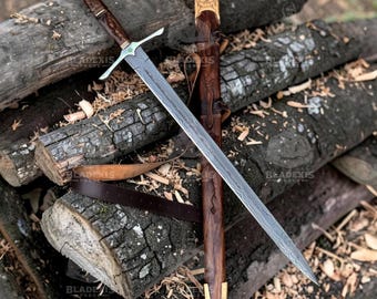 May include: A long, ornate sword with a patterned blade and a wooden handle, resting on a pile of logs. The sword has a silver crossguard and a matching pommel. A leather sheath with gold accents and a brown leather belt are also present.