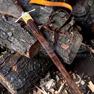 May include: A handcrafted sword with a dark wooden handle and blade, featuring intricate carvings and gold accents. The sword rests on a wooden surface with a leather strap. The blade measures approximately 30 inches.