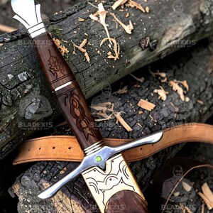May include: A detailed image of a sword with a wooden handle and a silver blade. The handle is intricately carved with a dark brown finish, and the blade is silver. The sword rests on a wooden surface.