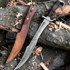 May include: A Damascus steel knife with a curved blade, a dark handle featuring a hooked pommel, and a silver crossguard. Beside the knife lies a brown leather sheath with embossed geometric patterns and two metal snap fasteners.