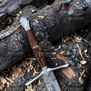 May include: A detailed image of a sword with a wooden handle and a silver blade. The handle is intricately carved with a dark brown finish, and the blade has a patterned design. The sword rests on a bed of weathered logs, showcasing a rustic aesthetic.