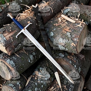May include: A long, silver sword with a blue handle and a black sheath. The sword is resting on a pile of wooden logs. The text "BLADEXIS FORGE" is visible on the image.