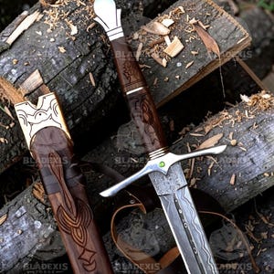May include: A detailed image of a sword and scabbard. The sword features a silver crossguard and a patterned blade. The handle is dark wood with intricate carvings. The scabbard is also wood, with leather straps and decorative carvings. The sword is resting on a pile of logs.