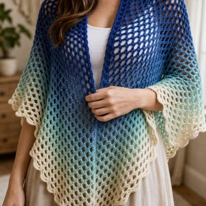 Puede incluir: Un chal de ganchillo azul, verde y crema. El diseño de tejido abierto presenta un efecto degradado, que pasa del azul oscuro al verde claro y crema. El chal tiene un borde festoneado.