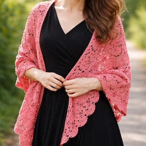 Può includere: Uno scialle color corallo a trama aperta con bordo smerlato. Lo scialle è drappeggiato su un vestito nero. Il design a trama aperta è visibile e lo scialle appare morbido e leggero. Lo sfondo è una scena esterna sfocata.