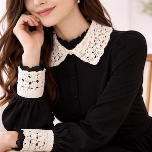 May include: Black dress with a white lace collar and cuffs. The long-sleeved dress features a button-down front and a flared skirt. The lace detailing adds a touch of elegance to the classic design. The dress is suitable for various occasions.