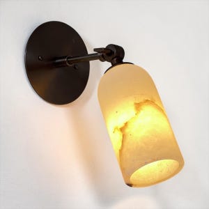 Può includere: Una tazza di ceramica bianca con un manico nero e la scritta "But First, Coffee" in nero, con un carattere a mano. La tazza è su una superficie bianca.
