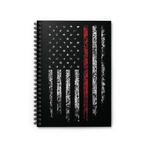 May include: A black spiral-bound notebook featuring a distressed American flag design. The flag has white stripes and stars, a red vertical stripe, and a textured, vintage appearance.