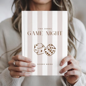 May include: A hardcover score book featuring a vertical striped pattern in white and light beige. The cover displays the text THE JONES GAME NIGHT and SCORE BOOK in brown, accompanied by a brown line art illustration of two dice.