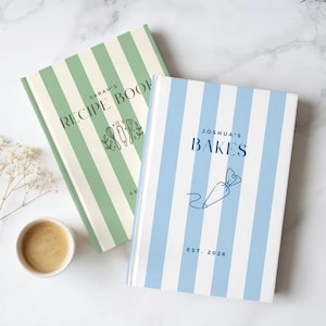May include: Two hardcover books with vertical stripes. One book is sage green with the text "SARAH'S RECIPE BOOK" and a rolling pin icon. The other is light blue with the text "JOSHUA'S BAKES" and a piping bag icon, both featuring "EST. 2026".