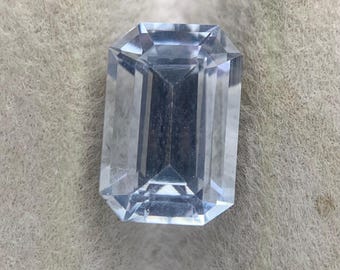 Peut inclure: Une pierre précieuse transparente et incolore taillée en forme d'émeraude rectangulaire avec des bords facettés. La pierre présente une grande transparence et une réflexion interne de la lumière, révélant un agencement géométrique.
