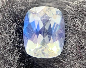 Peut inclure: Une pierre précieuse taille coussin à l'aspect translucide, affichant des éclats iridescents de lumière bleue, jaune et blanche sur sa surface à facettes. La pierre présente une qualité claire et réfléchissante avec des facettes géométriques.