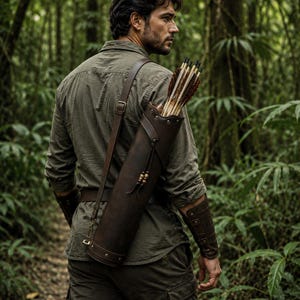 May include: A dark brown leather quiver with metal rivets and an adjustable shoulder strap, containing several arrows with feathered fletching. The quiver features decorative leather ties with wooden beads and is worn over an olive green shirt.