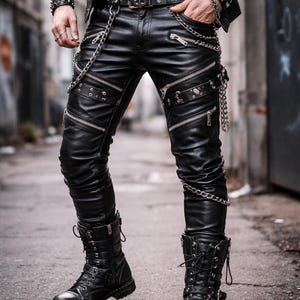 Op de afbeelding: Zwarte leren broek met meerdere ritsen en zilveren kettingaccenten. De broek wordt gecombineerd met zwarte combat boots en een riem met studs en een gesp in de vorm van een schedel. Rock- of alternatieve mode.