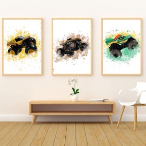 May include: Three framed prints showcasing monster truck illustrations in a watercolour style. The trucks are in yellow, black, and green, with colour splashes. The prints are displayed above a wooden console.