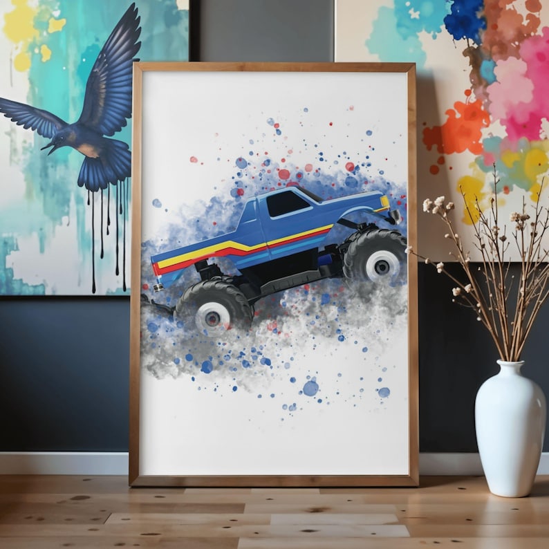 May include: A framed print of a blue monster truck with yellow and red stripes, depicted in motion. The artwork uses a watercolour effect with blue, red, and grey paint splatters. The frame is a light brown colour.