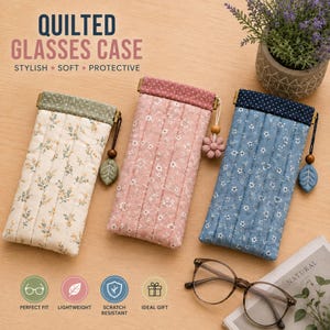 Pode incluir: Três estojos acolchoados retangulares para óculos nas cores creme, rosa e azul, cada um com um padrão floral e uma faixa superior de cor sólida com um pequeno pingente. O estojo creme tem um pingente de folha verde, o rosa uma flor e o azul uma folha.