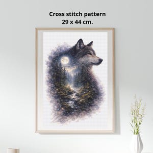 May include: Framed cross stitch pattern featuring a wolf with a forest and moon scene. The artwork is 29 x 44 cm (11.4 x 17.3 inches) and is displayed in a light-colored wooden frame. The wolf is depicted in shades of gray and brown.