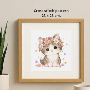 May include: A framed cross-stitch pattern featuring a cute gray and white kitten wearing a flower crown. The artwork is 23 x 23 cm (9 x 9 inches) and is surrounded by a light brown wooden frame. The kitten is surrounded by small flowers.