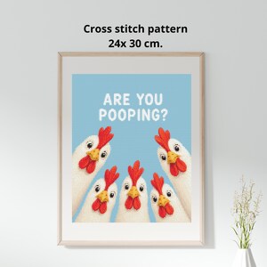 May include: A framed cross stitch pattern measuring 24x30 cm featuring four white chickens with red combs and wattles against a light blue background. The text ARE YOU POOPING? is printed in white block letters above the chickens.