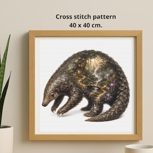 May include: A framed cross stitch pattern measuring 40 x 40 cm. The artwork features a pangolin with a detailed forest landscape integrated into its body, showing trees, a waterfall, and a path. The frame is light brown wood.