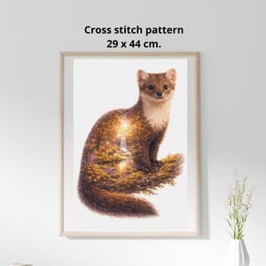 May include: Framed cross-stitch pattern featuring a brown and white animal with a detailed landscape design inside. The artwork measures 29 x 44 cm. The frame is a light wood color, and the background is white.