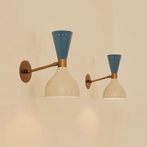 May include: Two mid-century modern wall sconces. Each has a blue conical top, a cream-coloured bell-shaped shade, and a brass-toned arm and wall mount. The shades have small, evenly spaced holes near the bottom.