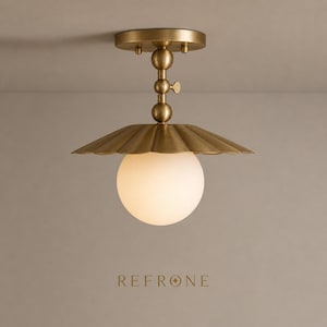 May include: A brass ceiling light with a scalloped shade and a spherical, frosted glass globe. The fixture has a decorative stem and a round ceiling mount. The word "REFRONE" is printed at the bottom.