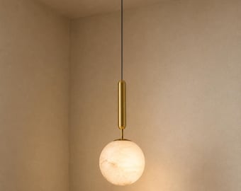May include: A pendant light featuring a spherical, translucent white stone shade suspended by a thin black cord. A cylindrical, brushed brass metal fixture connects the cord to the top of the globe, creating a clean, vertical, and balanced design.