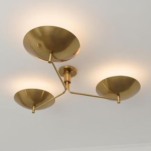 May include: A brass ceiling light fitting featuring three bowl-shaped shades. The shades are arranged on a branching structure, with a central mounting point. The light is on, illuminating the shades.