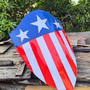 Puede incluir: Un escudo con una secci&oacute;n superior azul con tres estrellas blancas, que pasa a rayas verticales rojas y blancas. El escudo tiene una parte superior curva y una parte inferior puntiaguda, que recuerda un tema patri&oacute;tico.