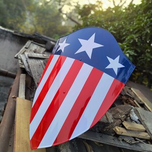 Puede incluir: Un escudo con una secci&oacute;n superior azul con tres estrellas blancas. La secci&oacute;n inferior tiene rayas rojas y blancas alternas. El escudo es ligeramente curvo y tiene un acabado brillante.
