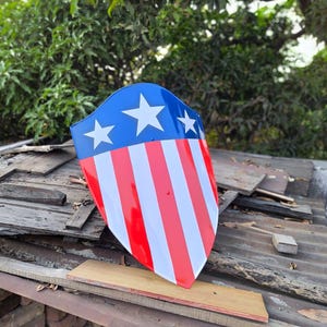 Puede incluir: Un escudo con una parte superior azul con tres estrellas blancas y rayas rojas y blancas. El escudo es un dise&ntilde;o patri&oacute;tico, que recuerda a la bandera estadounidense. El escudo est&aacute; hecho de un material brillante.